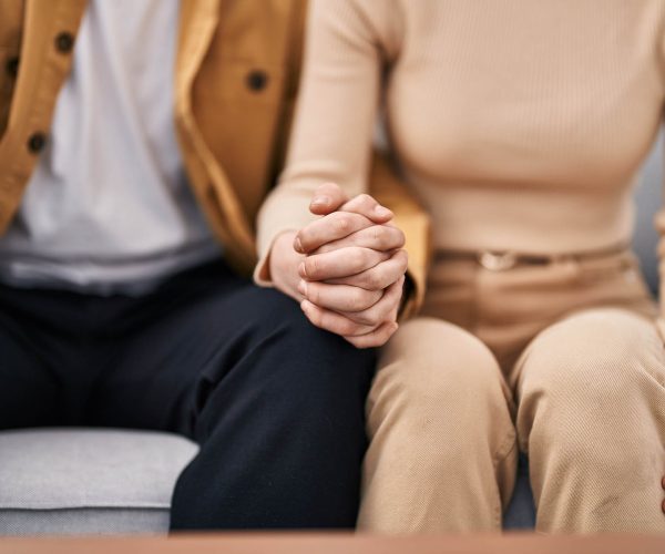 Mand and woman couple sitting on sofa with hands together at home