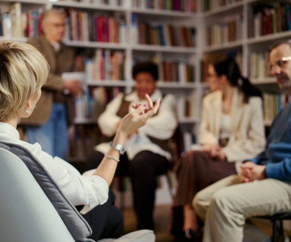 Middle aged woman leading group discussion with diverse adults during counseling session, back view. Useful for mental health, therapy, support group, communication campaigns